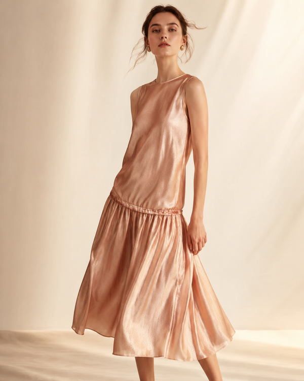 Model wearing an elegant drop-waist midi dress in soft rose-gold and blush tones, editorial studio lighting