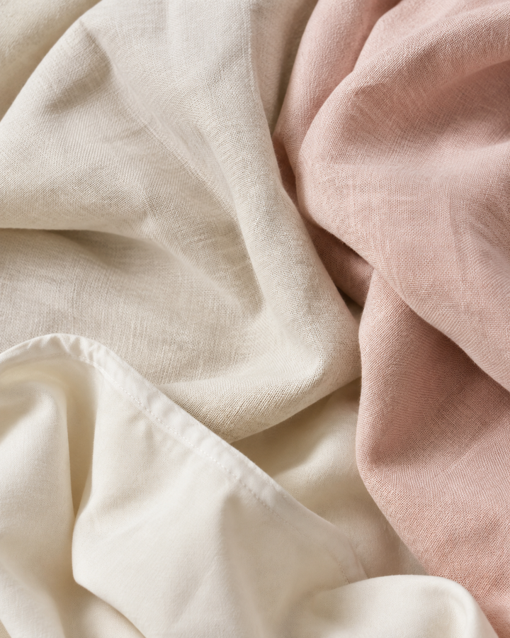 Close-up of natural linen and cotton fabric textures in cream and blush tones, eco fashion editorial